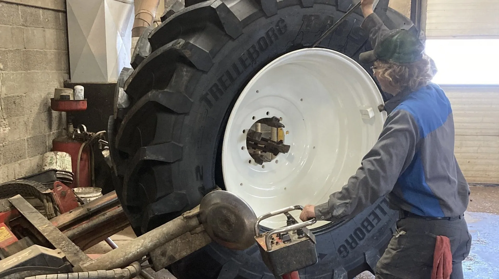 Mechanic in a shop mounting a large Trelleborg agricultural tire onto a white ag wheel using tire‑changing equipment, illustrating farm tire and on‑farm service for tractors and other agricultural equipment